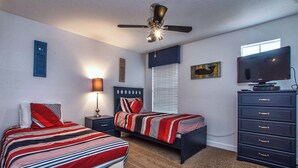 Une chambre avec deux lits, un ventilateur de plafond, une télévision et une commode.