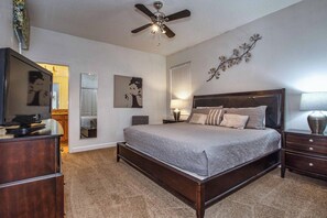 A bedroom with a bed, a ceiling fan, a dresser, a mirror, and wall art.