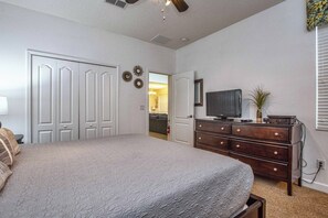 Une chambre à coucher avec un grand lit, une commode, un téléviseur et une porte donnant sur une autre pièce.