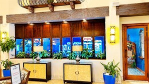 Un espace d’accueil avec un comptoir d’enregistrement, des plantes en pot et une vue sur les jeux d’arcade à travers la fenêtre.