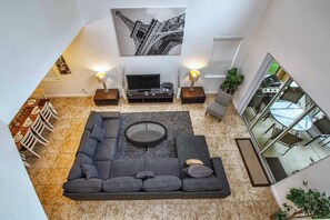 A modern living room with a sectional sofa, a flat-screen TV, and two side tables with lamps. - Spacious 5BR Paradise Palms Home with Private Pool & Loft (Kissimmee)