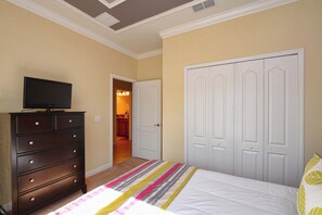A bedroom with a bed, dresser, television, and a closet.