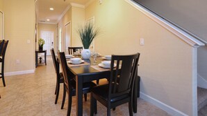 A dining room with a table set for four, chairs, a vase with flowers, and a staircase in the background.