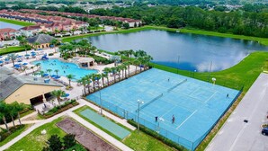 Ein großer Außenpoolbereich mit Tennisplatz, umgeben von Wohnhäusern und einem See.