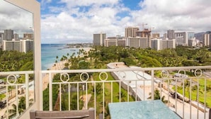 A balcony with a table and chairs, overlooking a cityscape with buildings and a beach.