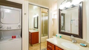 A bathroom with a built-in washer and dryer, a large mirror, and wooden cabinetry.