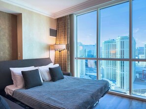 A hotel room with a large bed, a city view, and a floor lamp.