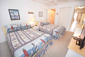 Un dormitorio con dos camas, un escritorio con computadora, una lámpara y un cuadro en la pared.