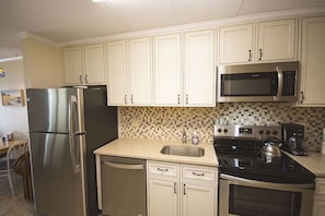 Una cocina con gabinetes blancos, electrodomésticos de acero inoxidable, salpicadero de azulejos y una cafetera.
