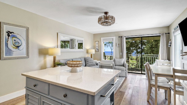 A modern kitchen with a large island, a dining area with a table and chairs, and a balcony with a view of the sea. - Gorgeous Beachfront Retreat! Heated Oceanfront Pool (Hilton Head Island)