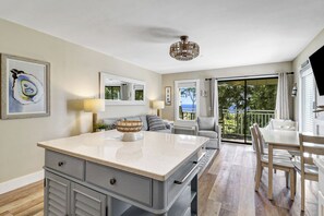 Et moderne køkken med en stor ø, et spiseområde med bord og stole, samt en balkon med havudsigt.