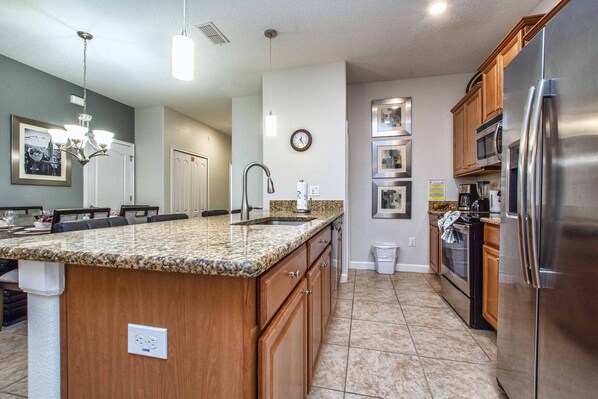 A kitchen with granite countertops, stainless steel appliances, wooden cabinets, and a built-in island. - Minutes to Disney | Private Pool, Resort Amenities & BBQ Grill - 1600ST (Kissimmee)