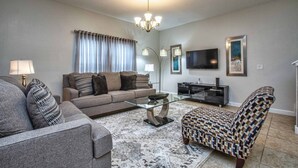 Una sala de estar con sofá, sillón, mesa de centro y televisor.