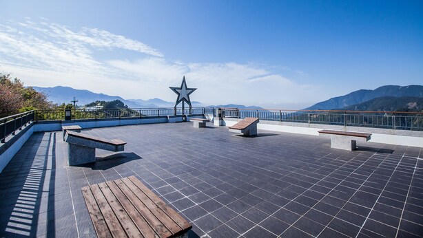 Terraço no telhado com um monumento em formato de estrela, bancos e guarda-corpo com vista para montanhas.