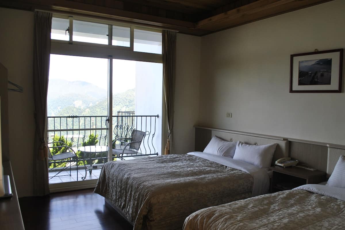 A hotel room with two beds, a balcony with a chair, and a framed picture on the wall.