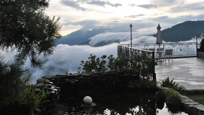 Um terraço com parede de pedra, um pequeno lago com um objeto flutuante e um corrimão com cadeiras.