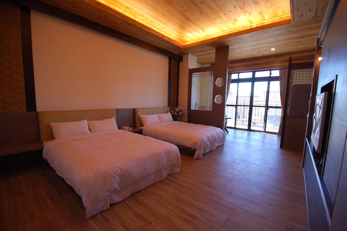 A hotel room with two beds, wooden flooring, a large window with a view, and a wooden ceiling.