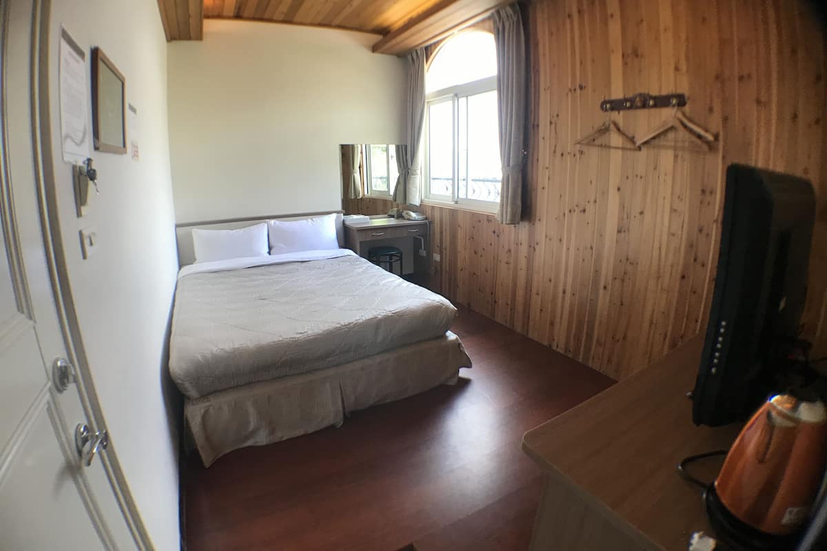 A room with a bed, a desk, a chair, a mirror, and a window.