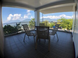 Un balcón con mesa y sillas, que ofrece vistas a montañas y árboles.