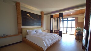 Um quarto espaçoso com uma cama grande, cabeceira de madeira, um quadro acima da cama e vista para o exterior através de uma janela ampla.