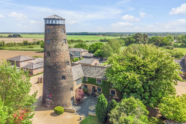 Una casa torre amb turó, envoltada per un pati i edificis adjacents, situada en un paisatge rural.