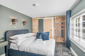 Een moderne slaapkamer met een bed, twee wandlampen, een bakstenen muur, een deur en een raam met zonwering.