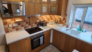 A modern kitchen with wooden cabinets, a built-in oven, a microwave, and a large window providing a view of the outside. - Character cottage (18c) on the edge of historic Belper (Belper)