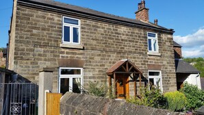 A two-story stone house with a traditional design, featuring a wooden front door and a small porch. - Character cottage (18c) on the edge of historic Belper (Belper)
