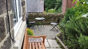 A small outdoor patio with a wooden bench, a round table, and two chairs. - Character cottage (18c) on the edge of historic Belper (Belper)