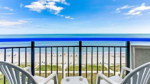 A balcony with white plastic chairs and a view of a beach with umbrellas and people. - Boardwalk Resort by Hosteeva (Myrtle Beach)