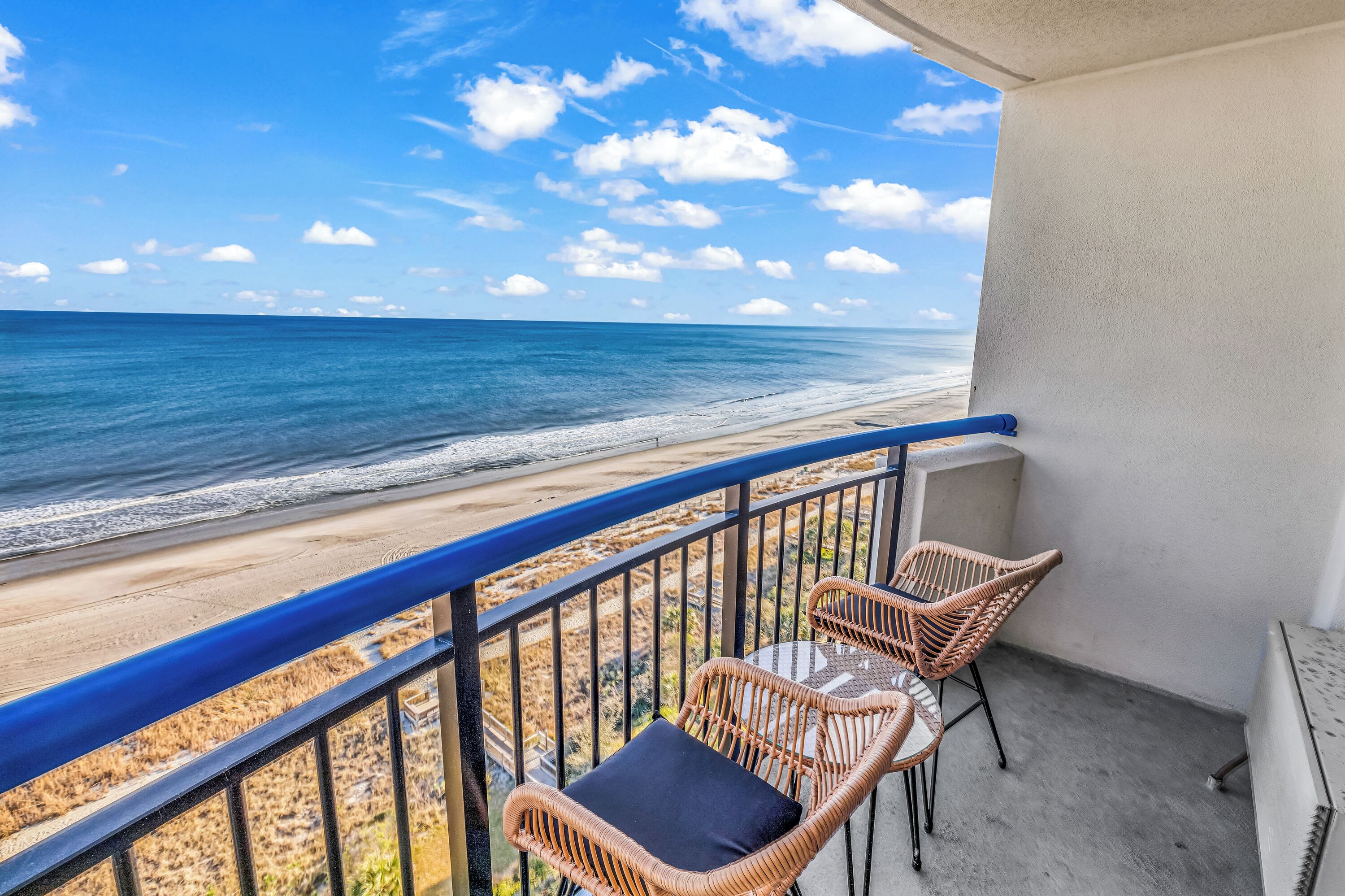A balcony with wicker chairs and a view of the beach and ocean.