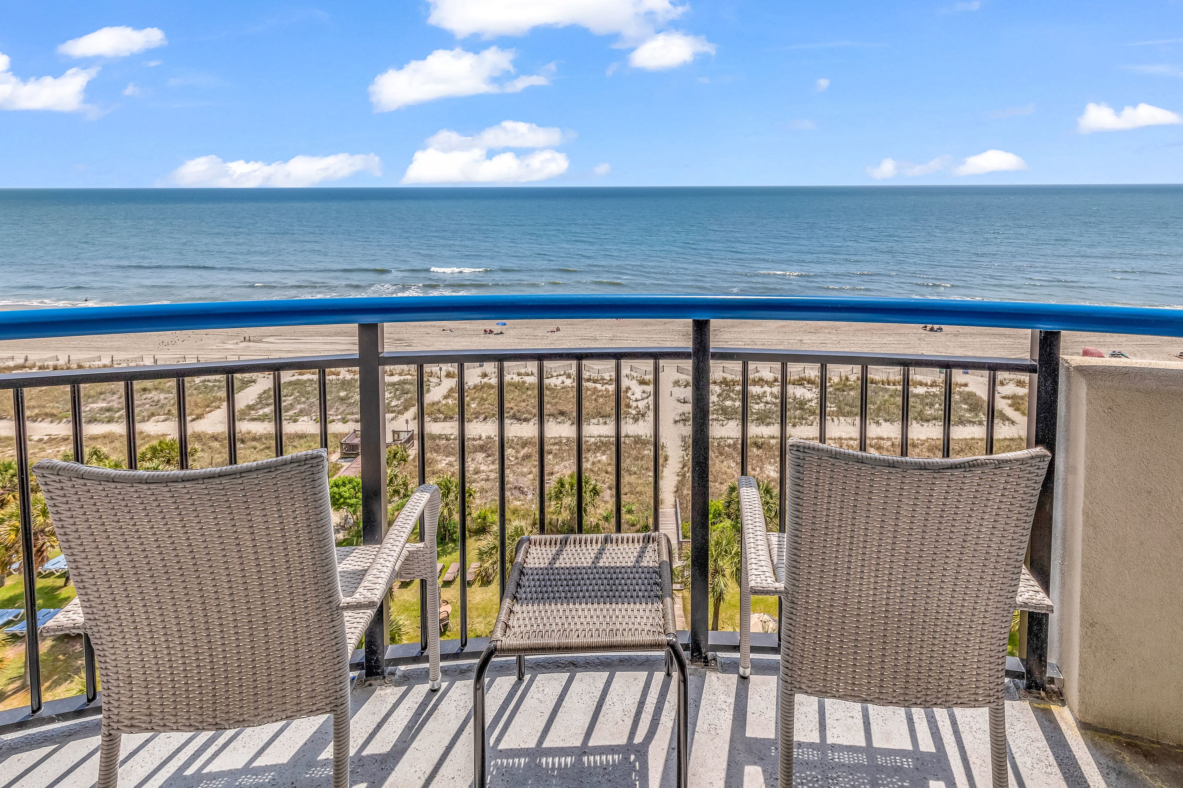 Ein Balkon mit Korbstühlen mit Blick auf Strand und Meer.