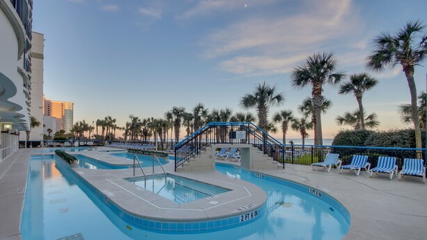 A swimming pool with blue tiles, palm trees, and lounge chairs. - Boardwalk Resort by Hosteeva (Myrtle Beach)