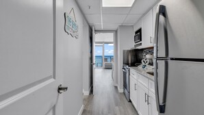 A narrow kitchen with white cabinets, a stainless steel refrigerator, and a microwave. - Boardwalk Resort by Hosteeva (Myrtle Beach)