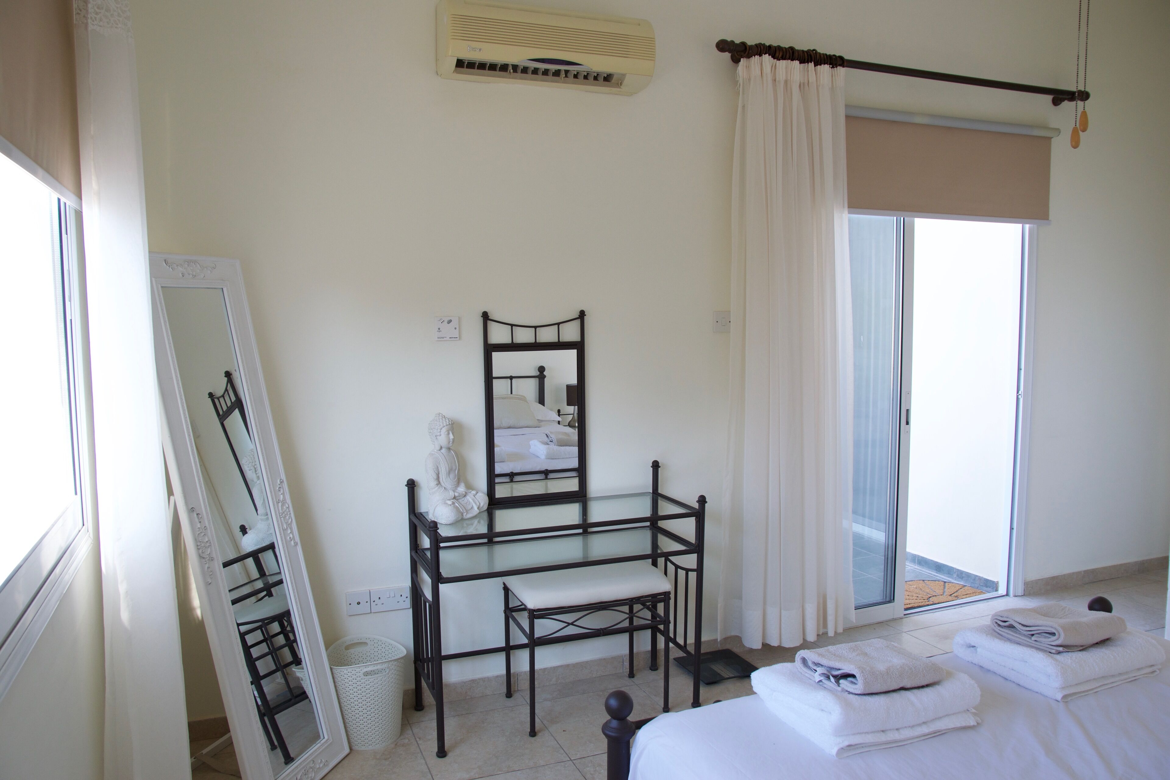 A bedroom with a bed, a glass desk, a chair, a mirror, and a window with curtains.