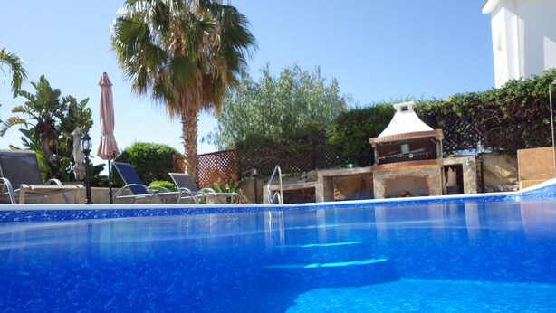 A clear blue swimming pool with lounge chairs and umbrellas, surrounded by greenery and a white building. - Villa, sea views, FREE A/C, pool, roof terrace, Wifi (Peyia)