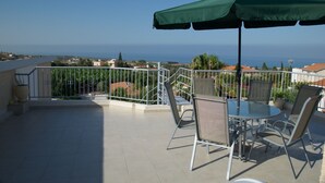 A balcony with a table and chairs, a green umbrella, and a view of the sea. - Villa, sea views, FREE A/C, pool, roof terrace, Wifi (Peyia)
