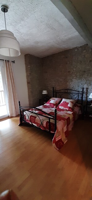 Ein Schlafzimmer mit Holzboden, einem Metallbettgestell und einer rot-weißen Bettdecke.