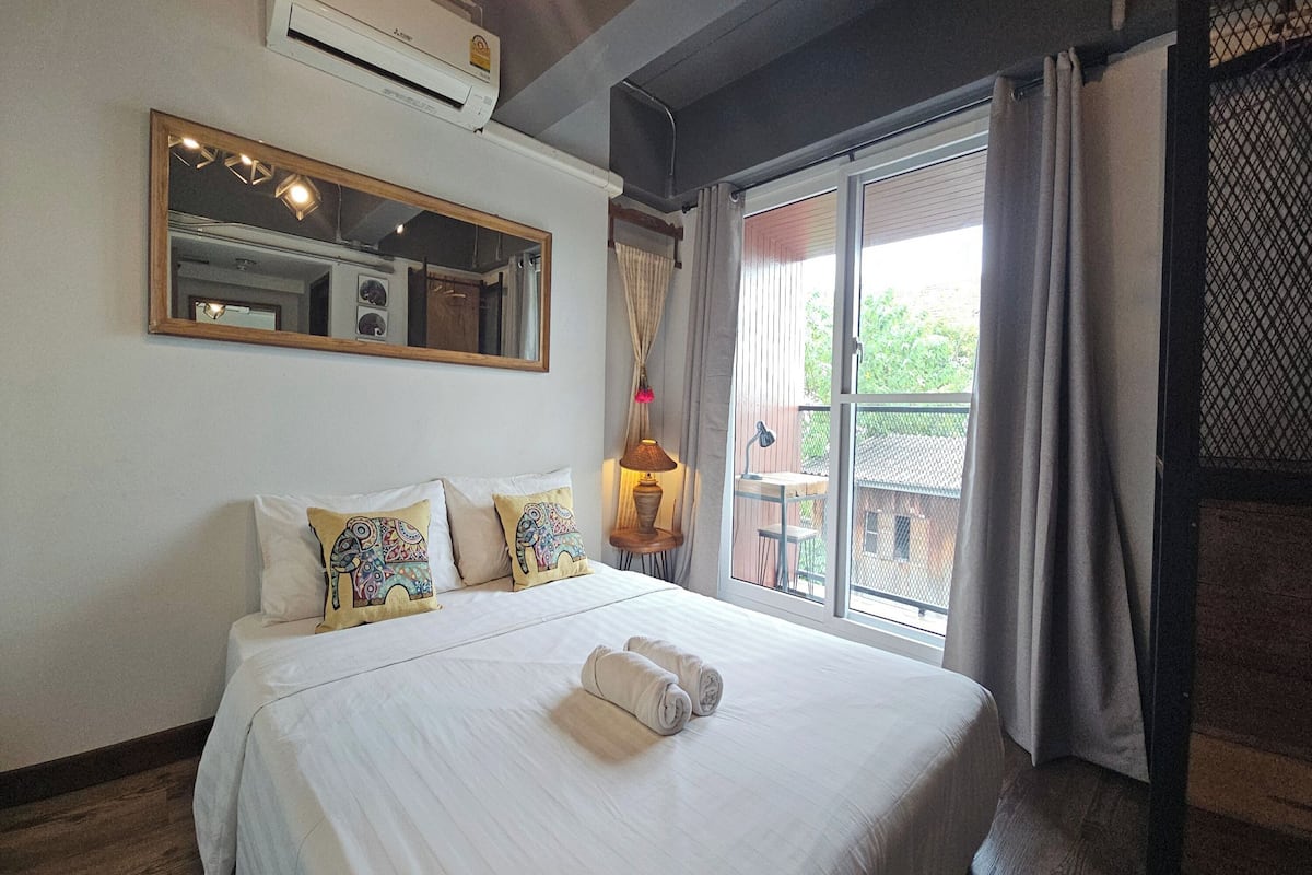A hotel room with a large bed, a mirror, a window with curtains, and a view of the outdoors.