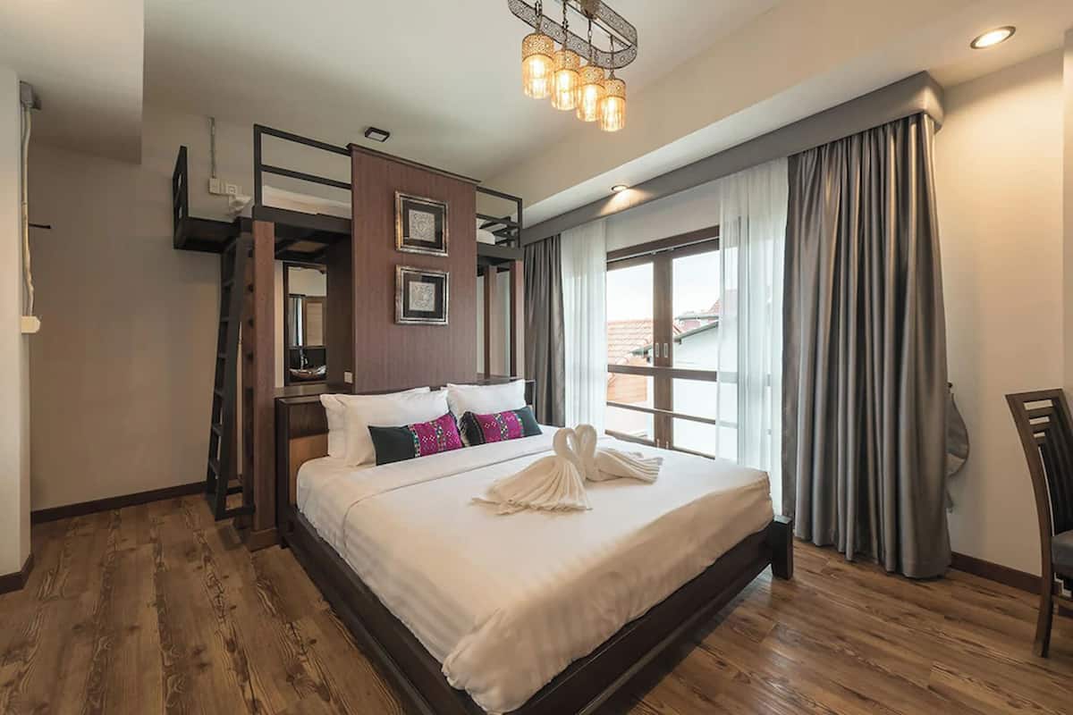 A hotel room with a large bed, wooden flooring, a bunk bed, and a view of the outside.