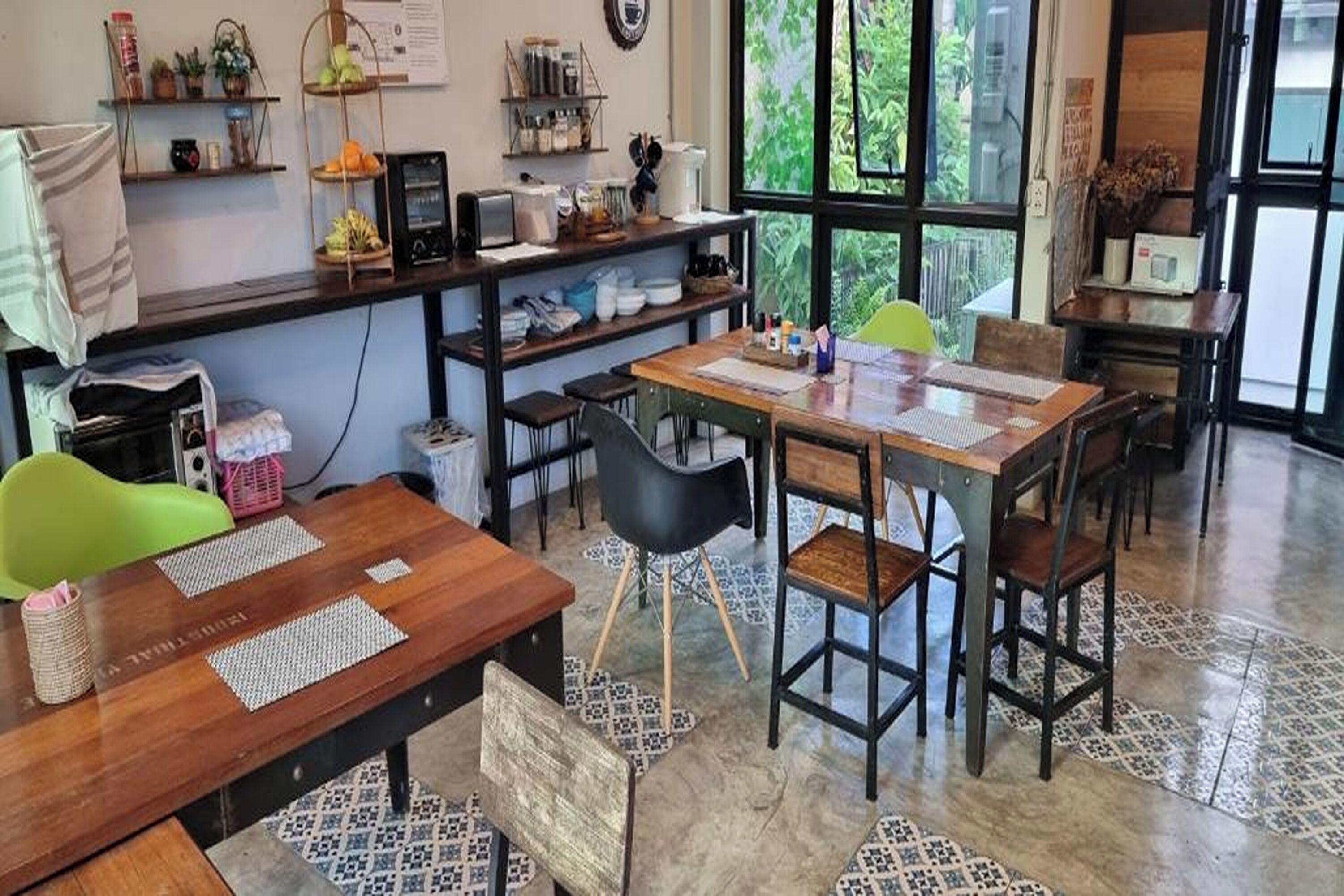 A cozy cafe with wooden tables and chairs, a coffee machine, and shelves with jars and plants.