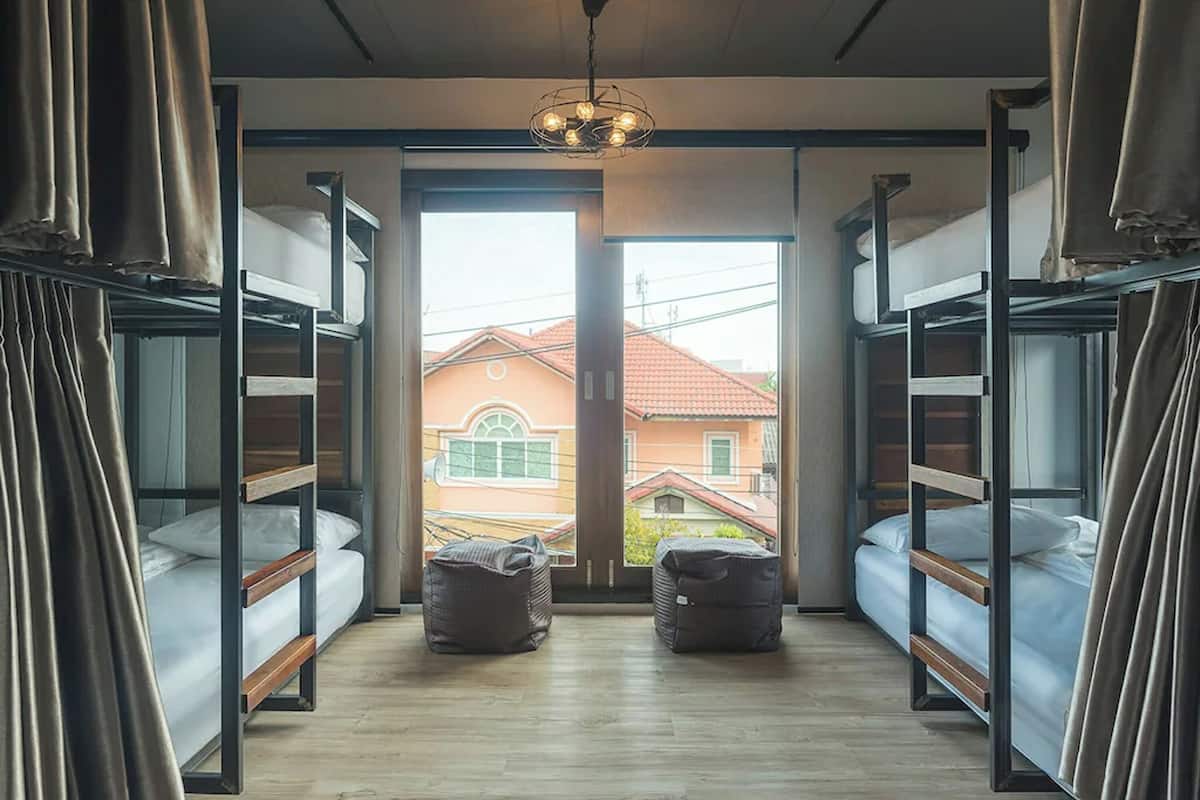 A dormitory room with bunk beds, a wooden floor, and a view of buildings outside.