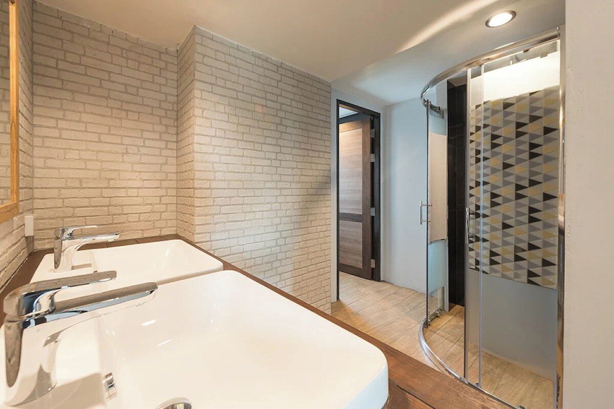 A modern bathroom with a large white sink, a mirror, and a shower with a geometric tile pattern.