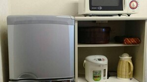 A compact kitchenette with a refrigerator, microwave, and a small cabinet with a kettle and a container. - Abiko Guest House (Osaka)