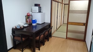 A small dining area with a wooden table, four chairs, a white refrigerator, and a blue kettle. - Abiko Guest House (Osaka)