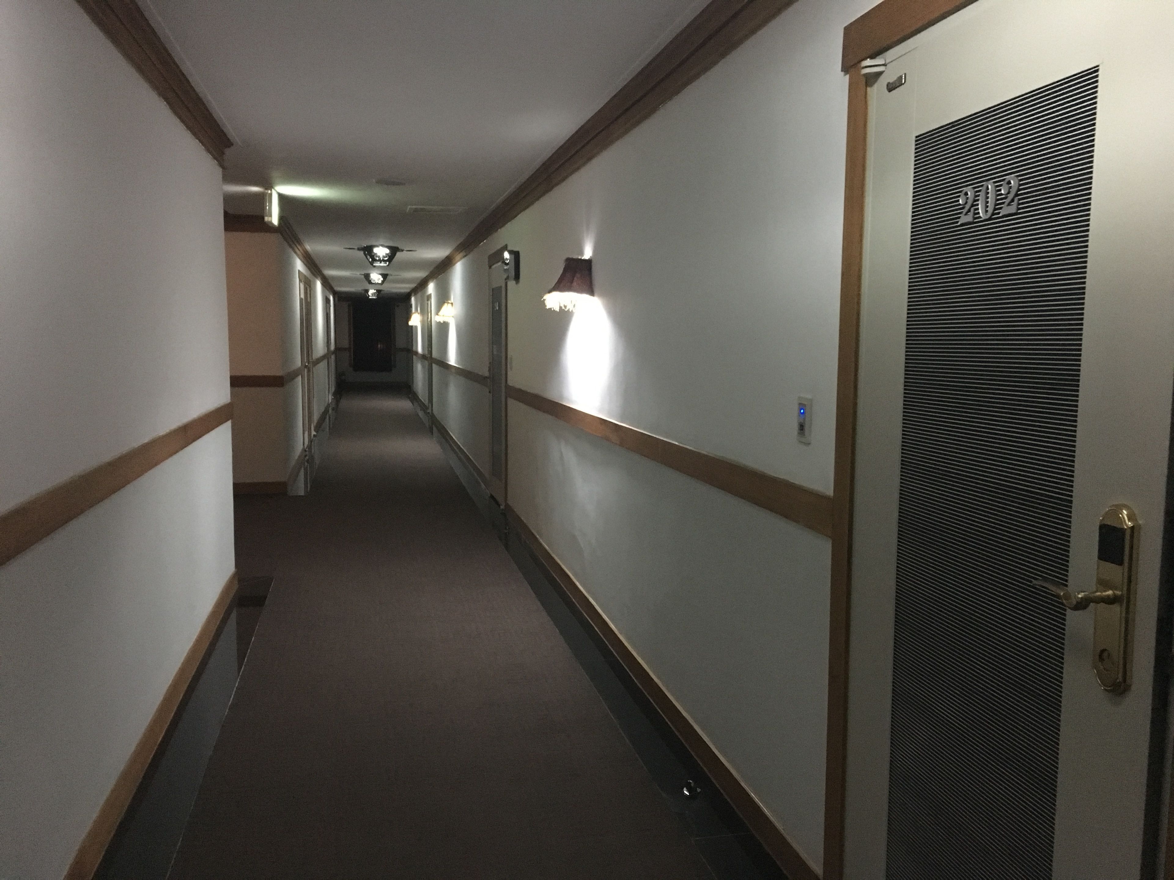 Ein Hotelkorridor mit Teppichböden, Holztäfelung und einer Tür mit der Nummer 202.