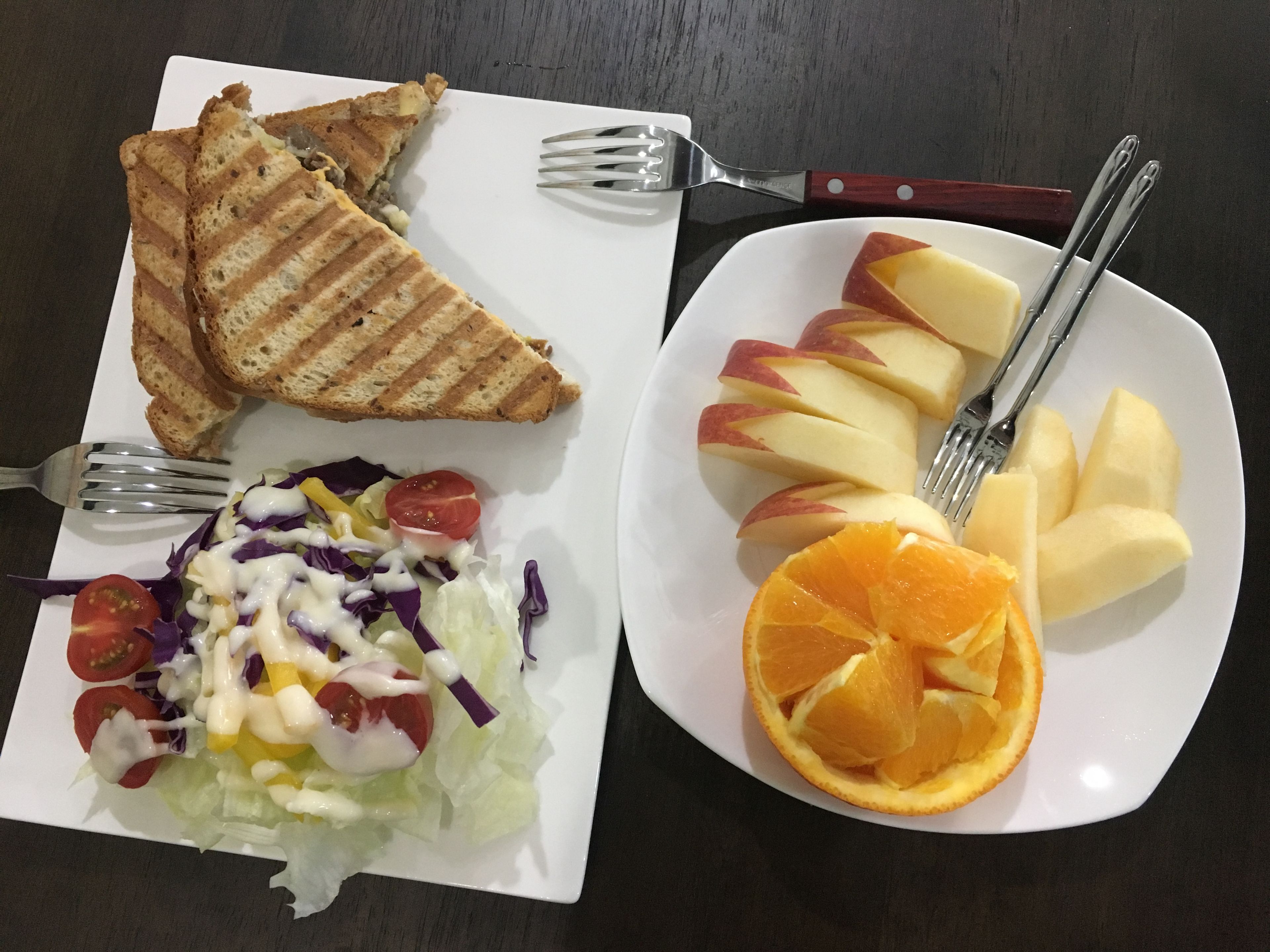 A plate with grilled toast, a salad, and sliced fruit including apples and oranges.