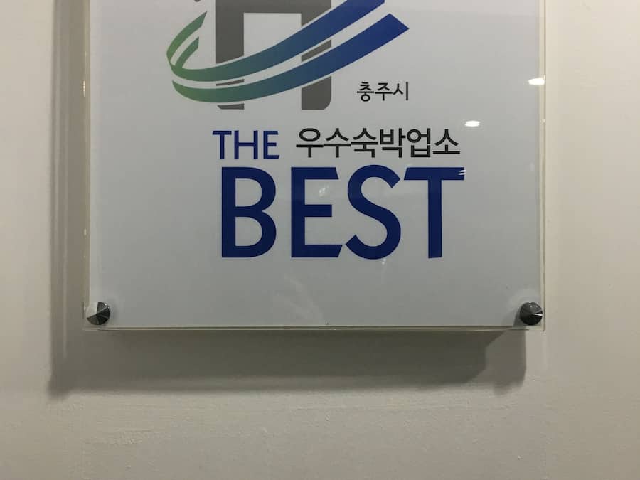 Un letrero con una imagen de una casa y un diseño ondulado, y texto en inglés y coreano.