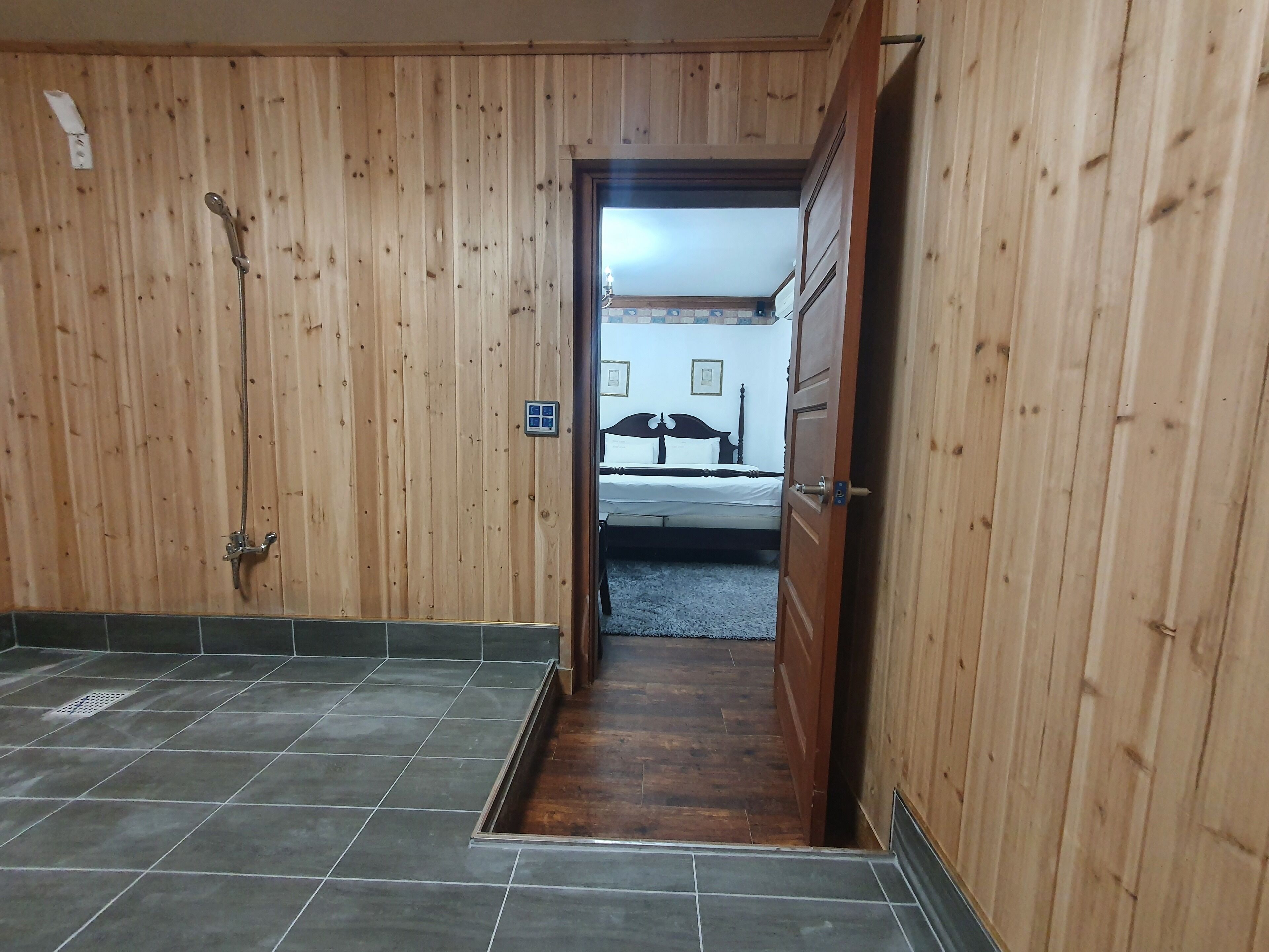 A wooden-paneled hallway leading to a bedroom with a bed and a nightstand.