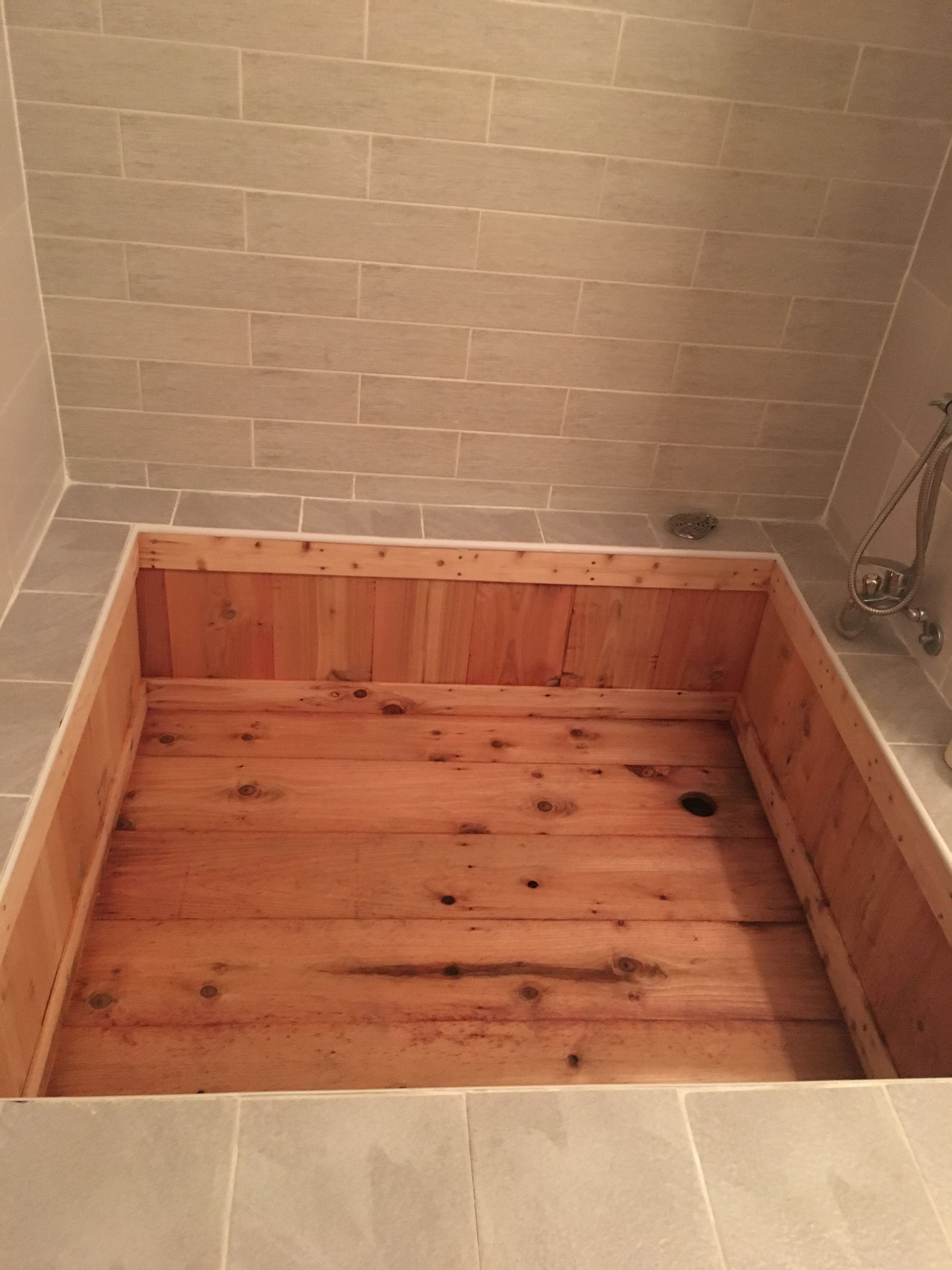 A wooden bathtub with a tiled shower area.
